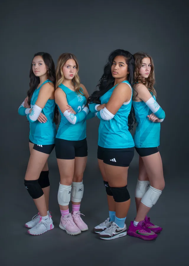 Four volleyball players in teal jerseys pose with crossed arms against a dark studio backdrop.